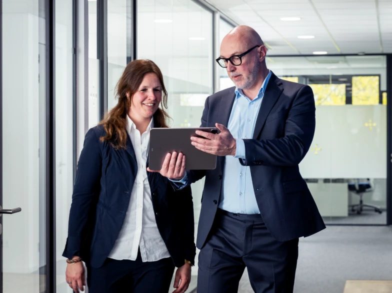Twee collega's lopen met een tablet door het kantoor